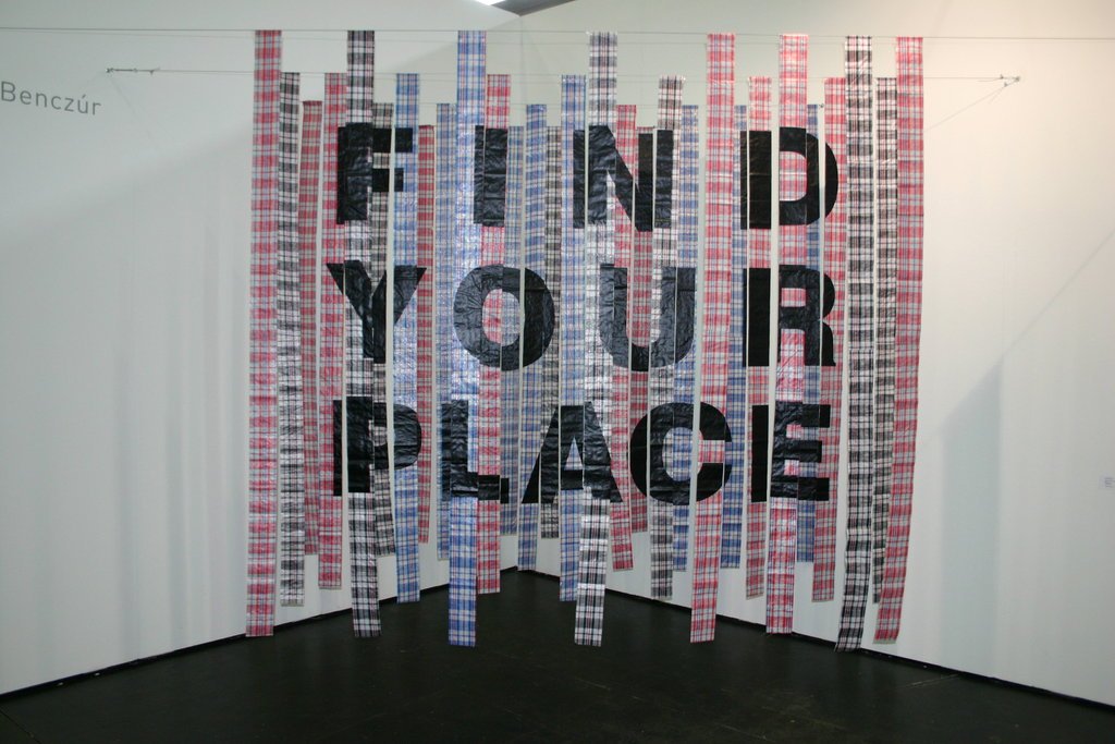 Image description: A large, hanging artwork by Emese Benczur that spells out "Find Your Place" in black letters on a striped backdrop