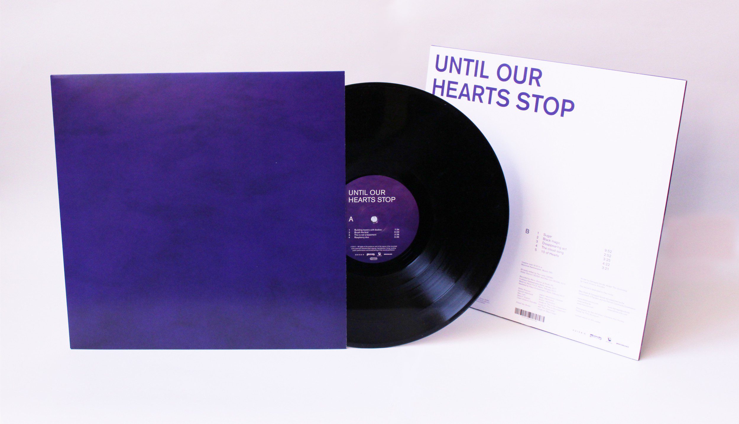 A black vinyl record partially out of a dark purple sleeve, with its white back cover displayed. The cover reads “UNTIL OUR HEARTS STOP” in large purple letters.