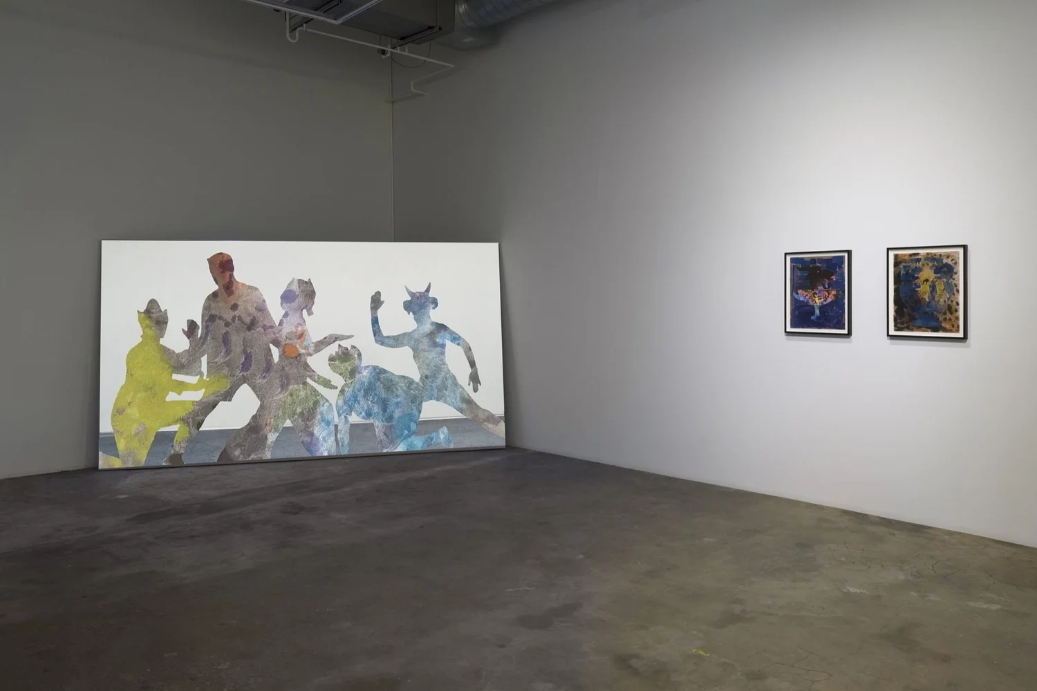 A minimalist gallery room displays a large artwork with colorful, abstract human silhouettes on the floor and two smaller framed paintings with dark backgrounds on the wall to the right.