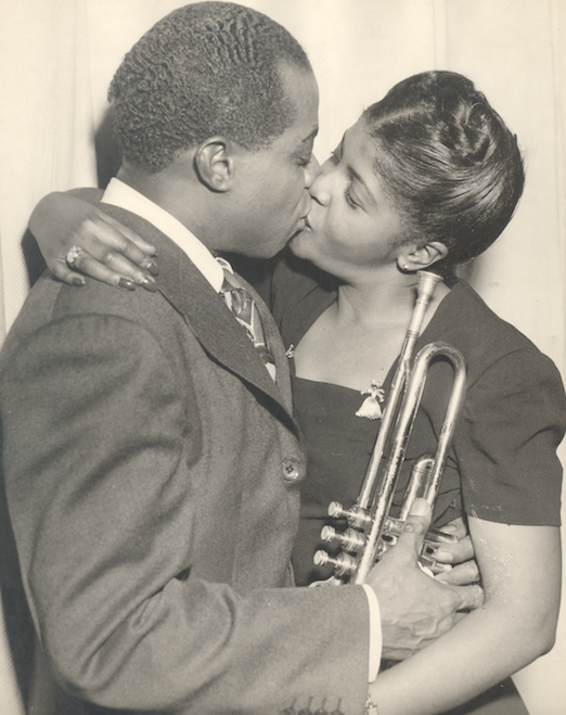 B&W photo of Louis & Lucille Armstrong embracing in a kiss, Louis holding a trumpet