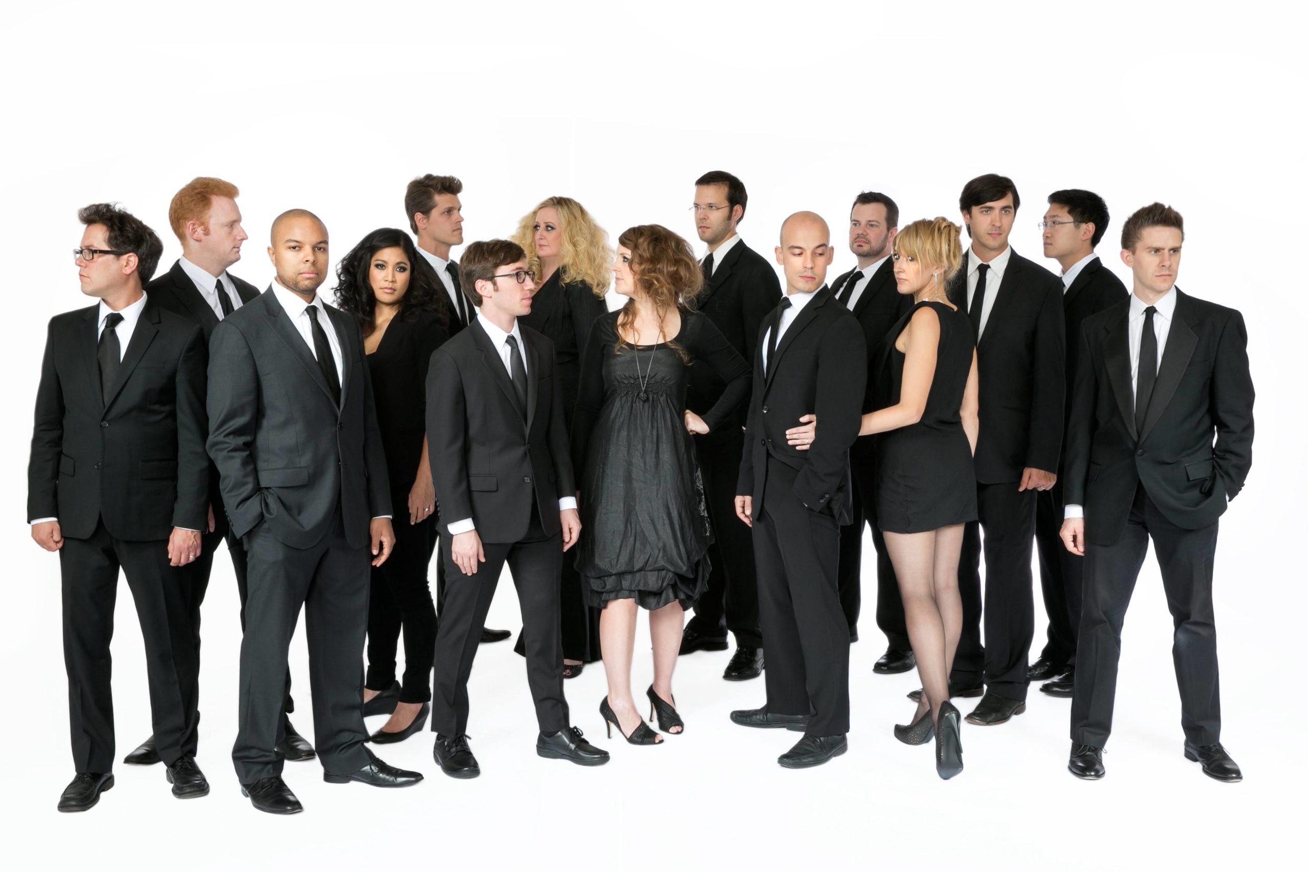 A group of people in black suits and dresses stand looking at one another.