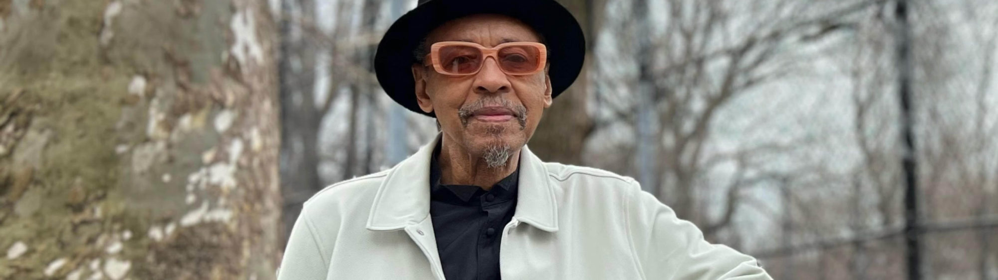 Henry Threadgill wearing pink sunglasses, a black hat, and a white jacket.