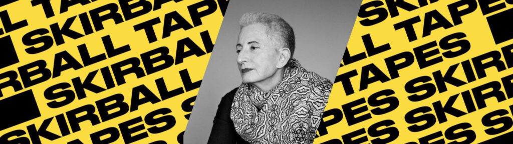 Black and white photo of an older person with short gray hair and a patterned scarf, centered on a background with yellow and black diagonal text reading “SKIRBALL TAPES.”.