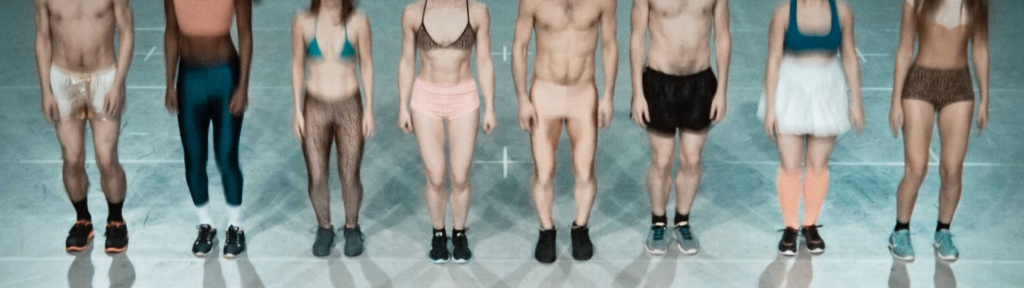 Eight people wearing various athletic outfits stand in a row, mid-jump, on a light-colored gym floor. Their heads are cropped out of the image, showing only their bodies from shoulders down.