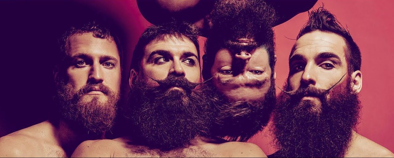 Four bearded men pose with serious expressions; three are upright while one is upside down, all against a purple and red background.