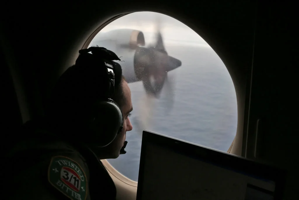 A person wearing headphones looks out an airplane window over the ocean, with a blurred propeller and part of a laptop visible in the foreground.