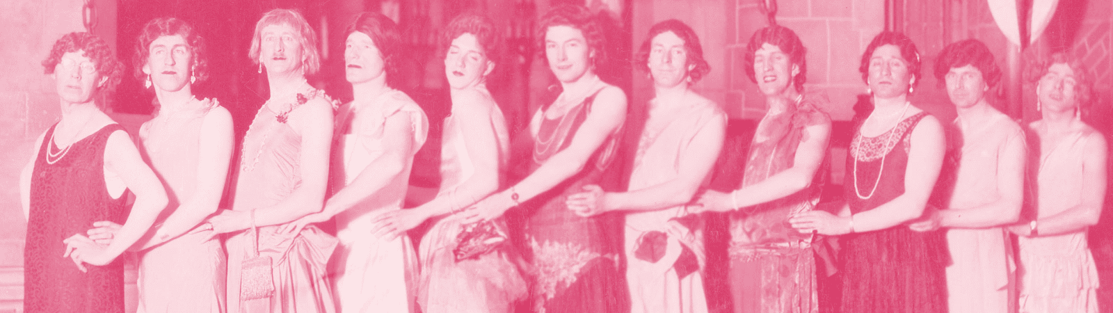 Ten people in dresses stand in a line, posing side by side with arms linked. The image has a pink tint and appears to be vintage.