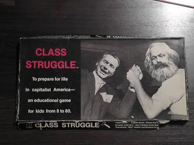 A board game box titled “Class Struggle” shows two men arm wrestling, one in a suit and one with a beard. Text reads: “To prepare for life in capitalist America—an educational game for kids from 8 to 80.”.