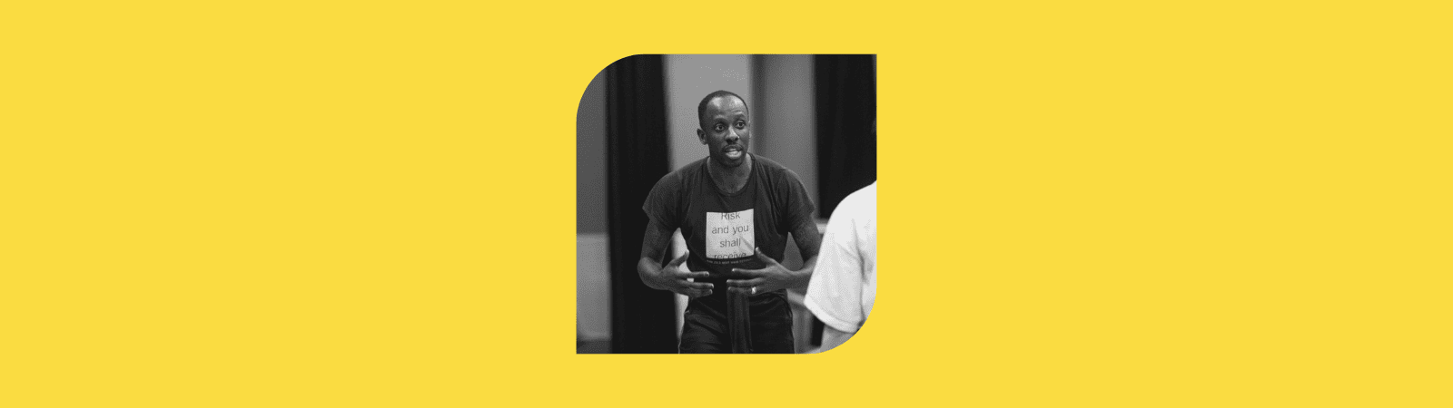 A person gestures passionately while speaking, wearing a dark T-shirt and standing indoors. The photo is black and white and placed on a solid yellow background.