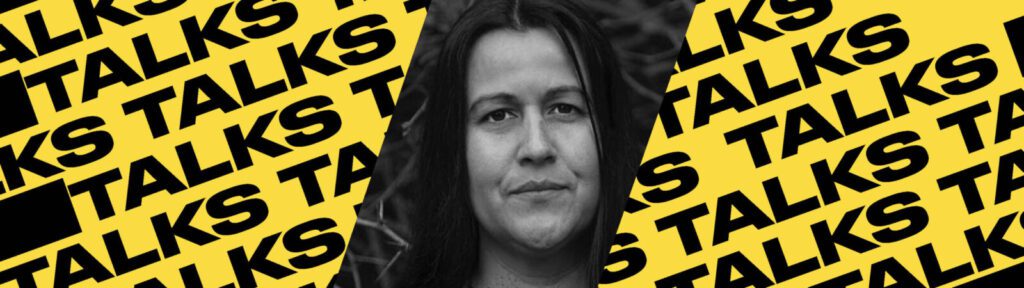 A black-and-white photo of a person is centered on a yellow background with the word “TALKS” repeatedly printed in bold black letters diagonally across the image.
