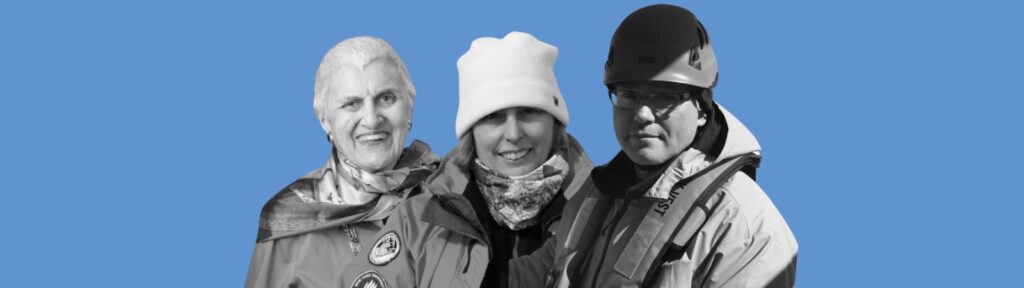 Three people dressed in cold-weather gear stand side by side, smiling. The background is solid blue. Two wear hats, and one person wears a helmet.