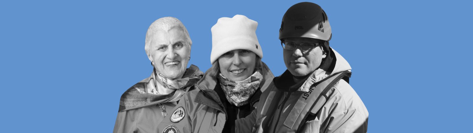 Three people dressed in cold-weather gear stand side by side, smiling. The background is solid blue. Two wear hats, and one person wears a helmet.