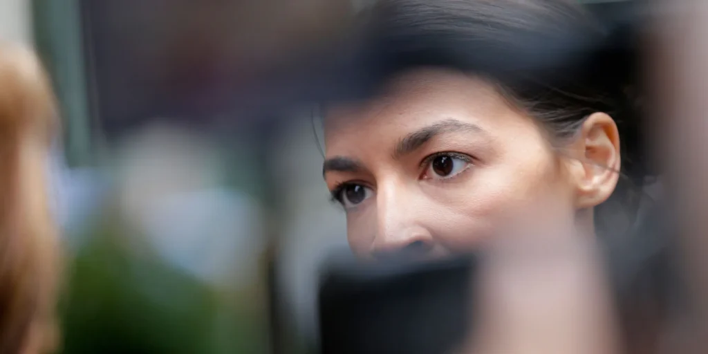 A close-up of a woman’s face, focused on her eyes as she looks intently forward, with blurred objects in the foreground partially obscuring her face.