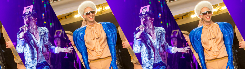 A person in a shiny blue and peach costume, white wig, sunglasses, and a card with a face on their forehead sings into a microphone on stage. The image is duplicated with a purple diagonal stripe overlay.