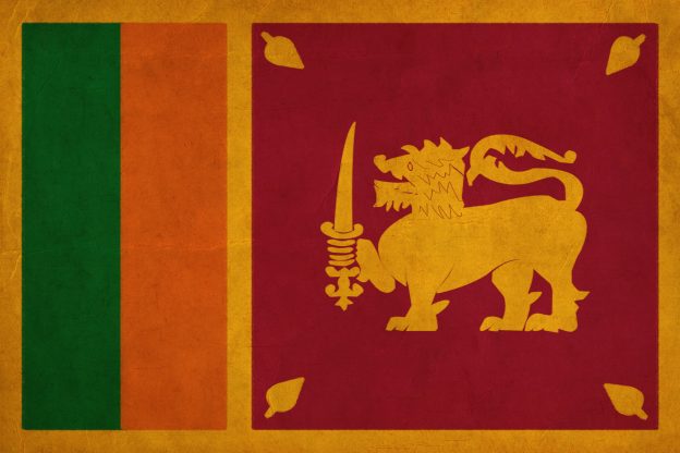 The flag of Sri Lanka features a gold lion holding a sword on a maroon background, with gold leaves in the corners, and vertical orange and green stripes on the hoist side.