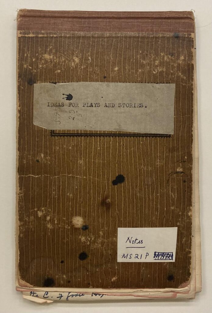 A worn brown notebook with a label reading “IDEAS FOR PLAYS AND STORIES.” Another white label reads, “Notes, MS21P.” The cover has stains, a fabric spine, and handwritten text at the bottom.