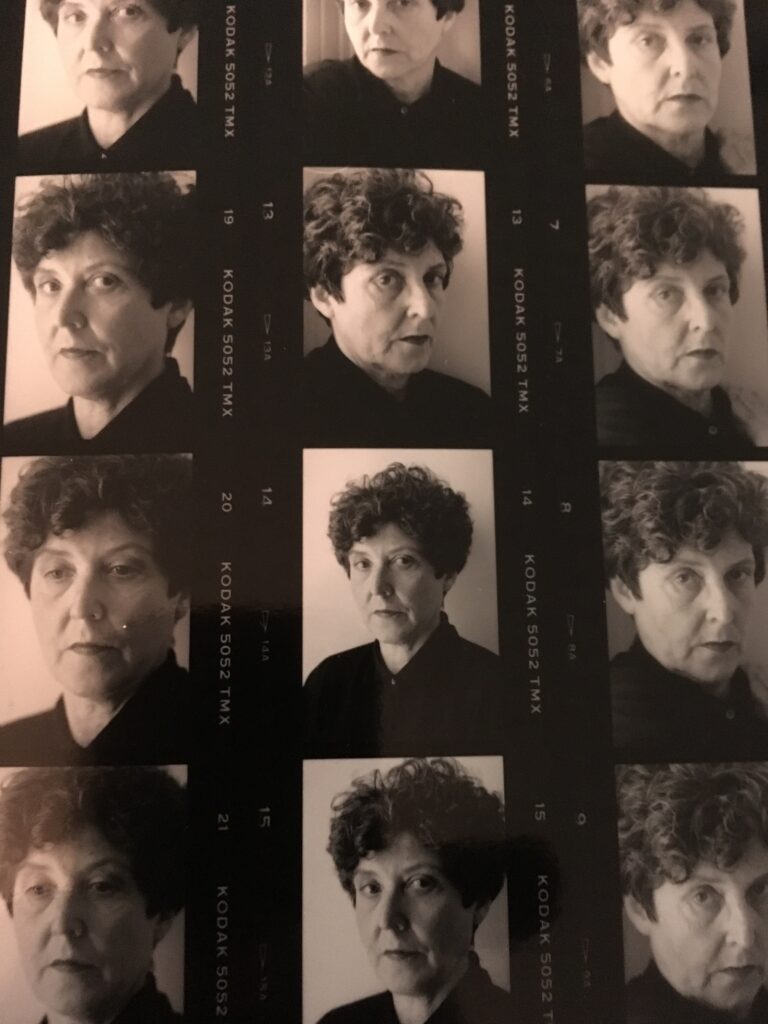 A black-and-white contact sheet featuring multiple portraits of the same person with short curly hair, wearing a dark top, posing with serious and neutral expressions in each frame.