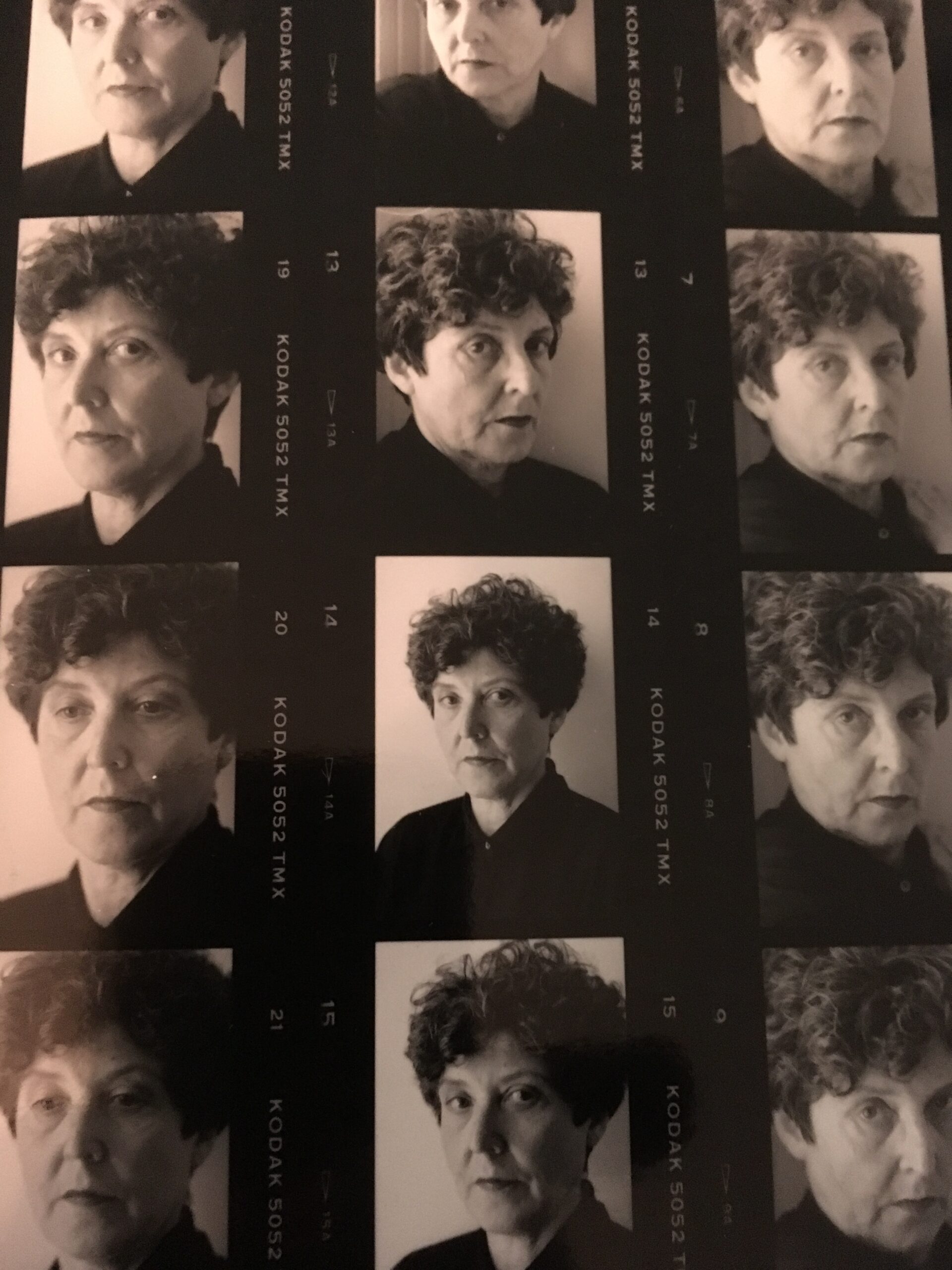 A black-and-white contact sheet featuring multiple portraits of the same person with short curly hair, wearing a dark top, posing with serious and neutral expressions in each frame.